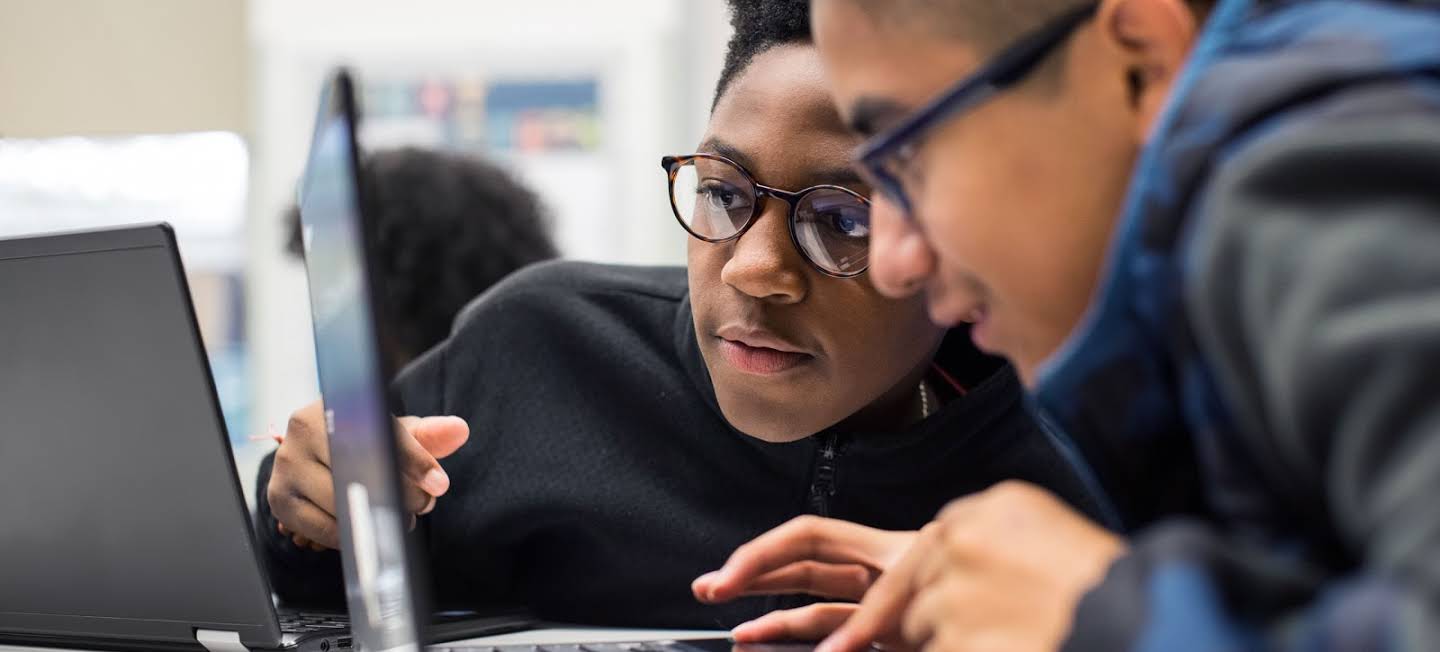 Two students lean in excitedly to collaborate on an assignment in Classroom.